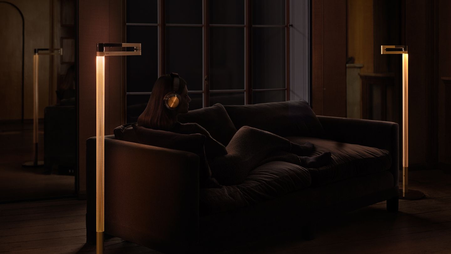 Напольный светильник Dyson Solarcycle Morph с тёплым свечением стойки у дивана, официальная фотография в другой отделке